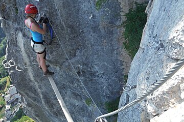a woman standing on a wooden plank half way up a rock face