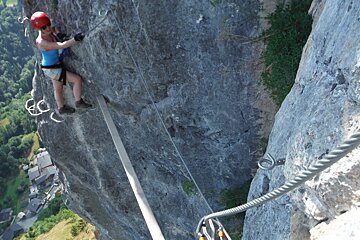 a woman climbing via ferrata in a red helmet