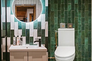 Vibrant green and white tiled bathroom featuring an illuminated mirror, a stylish sink, and a toilet with unique patterned paper.