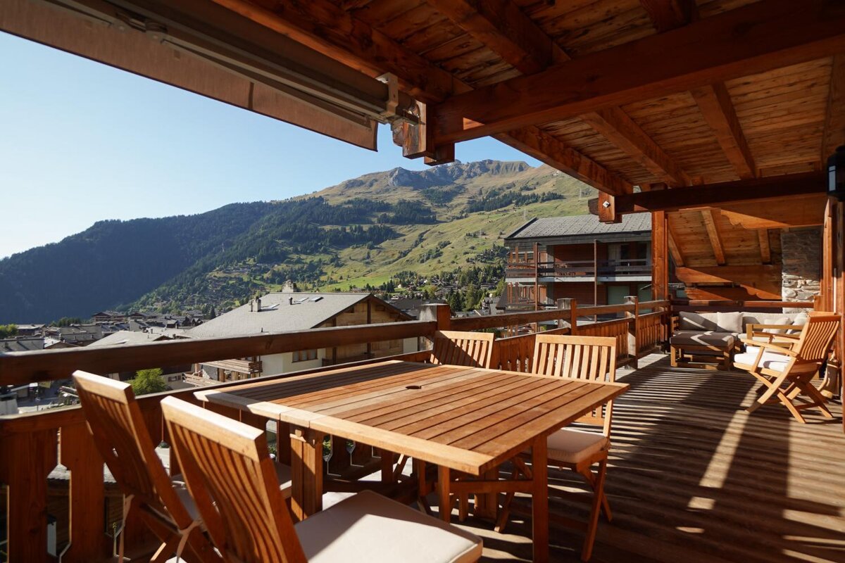 A wooden table and chairs on a balcony with mountains in the background