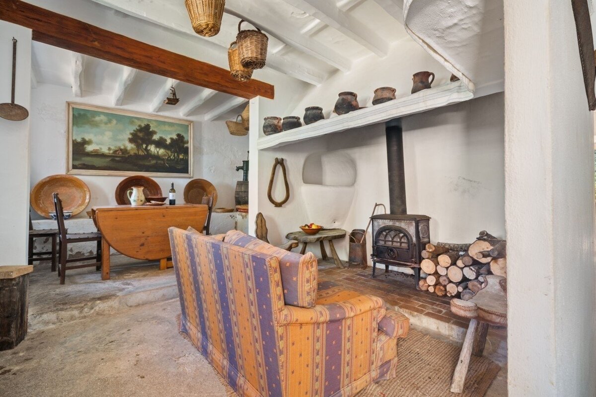 Cozy, rustic living space with a striped sofa, wood stove, dining table, and antique accents against whitewashed walls.