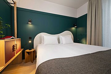 A bedroom with a bed a nightstand and a green wall