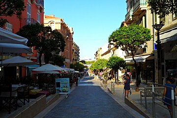 a shaded street with restaurants and shops on either side