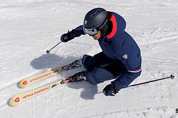 A skier in a blue snowsuit and helmet carves down a snowy slope.