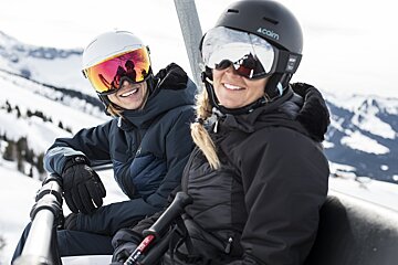 A woman wearing a coin helmet sits next to another woman