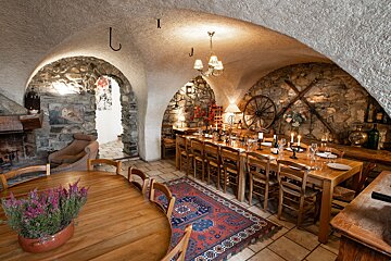 A cozy, rustic vaulted dining room with stone walls, a long wooden table set for guests, a fireplace, and traditional decor.
