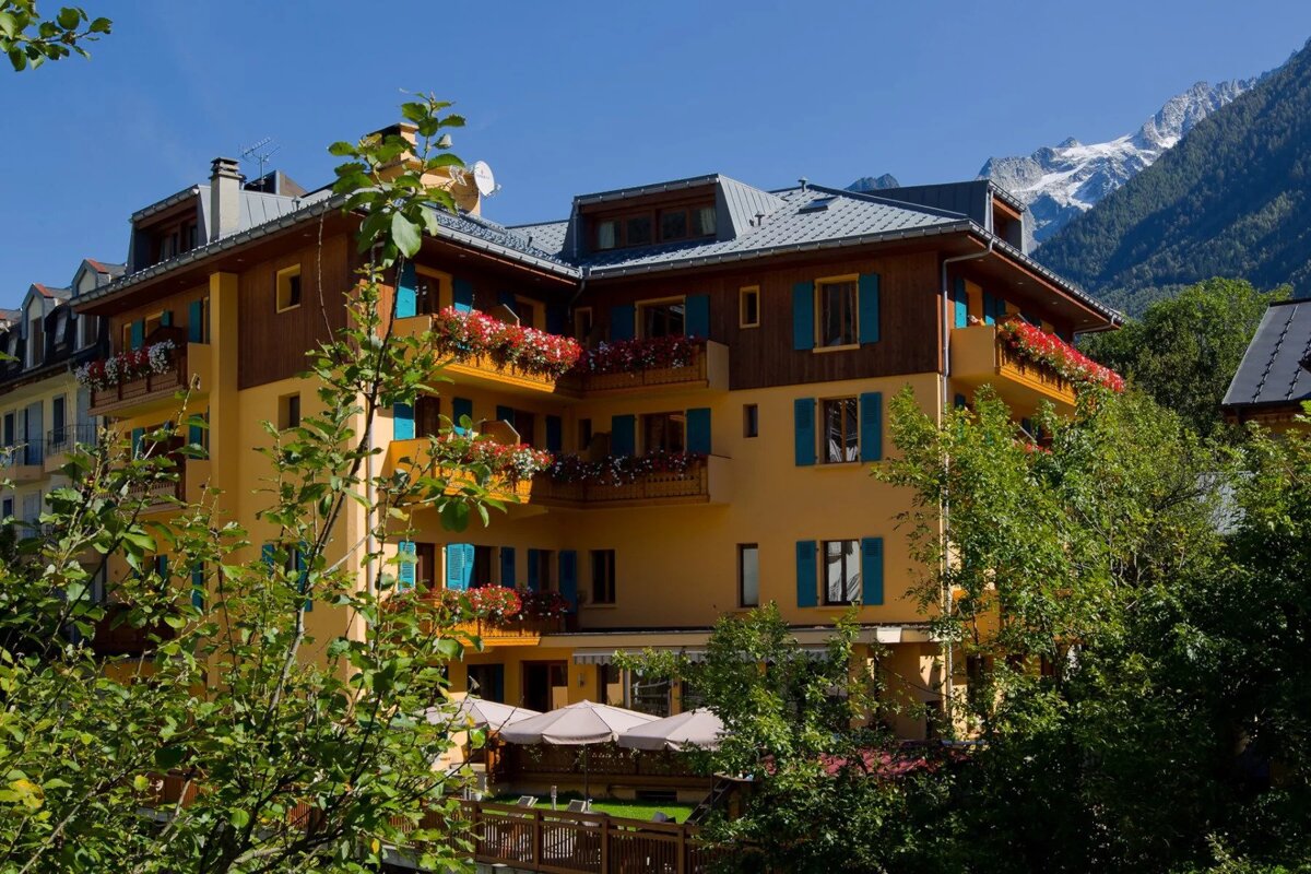 A yellow building with blue shutters and flowers on the balconies