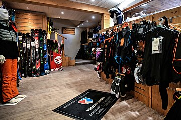 A ski shop interior with skis lined up, winter apparel on racks, a mannequin in ski gear, and a 