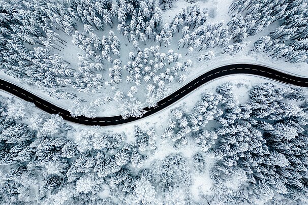 An aerial view of a road through a snowy forest