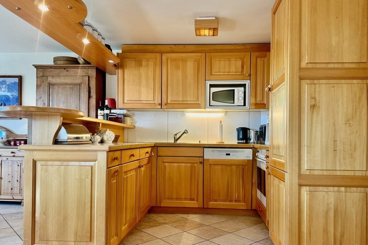 A cozy, light-wood kitchen featuring extensive cabinetry, an L-shaped counter with a sink and appliances, and a bar area with overhead lighting.