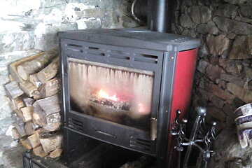 Wood burner, stack of logs, stone wall and gloves