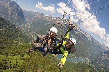 A man and a woman are parasailing over a mountain range