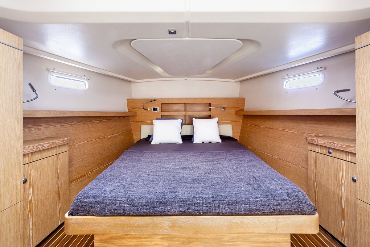Inside a modern yacht cabin featuring a double bed with wooden paneling, white pillows, and a blue cover.