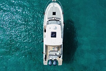 Aerial shot of a white boat with two outboard motors floating on clear, sparkling turquoise water.