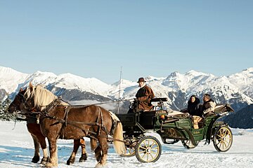 A horse drawn carriage in the snow with mountains in the background