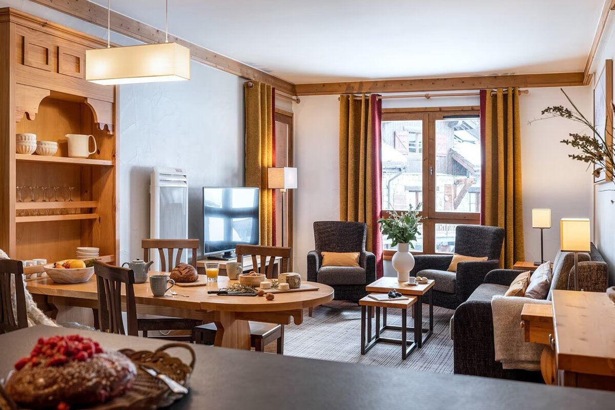 Cozy, rustic chalet interior featuring a wooden dining area and a comfortable living space with golden curtains.