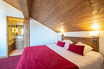 A bedroom with a wooden ceiling and a bed with red pillows