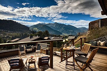 A wooden deck with chairs and a table with mountains in the background