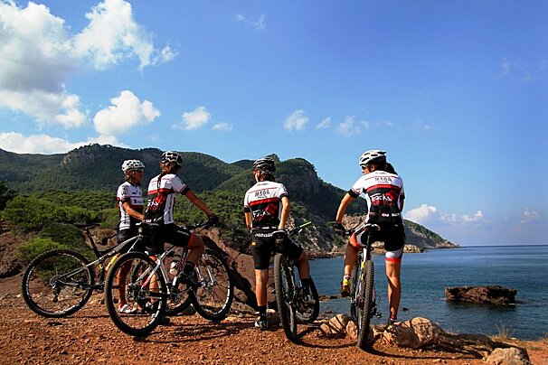 A group of cyclists are standing on a rocky hill overlooking the ocean