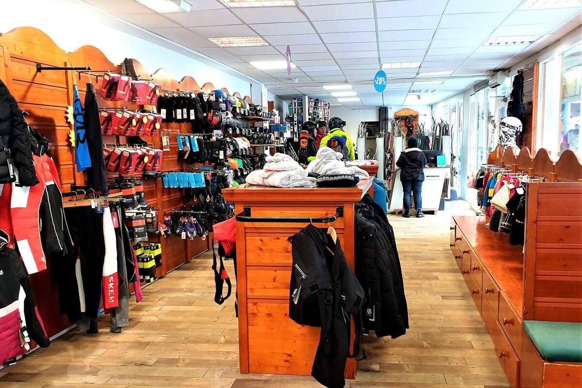 A brightly lit ski and winter sports shop filled with colorful apparel, gloves, and gear on wooden racks and displays, with customers browsing.