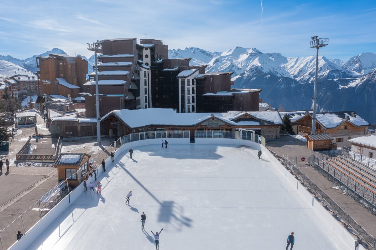 People are ice skating on a rink with mountains in the background