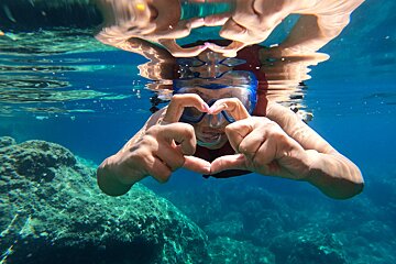 A person making a heart shape with their hands in the water
