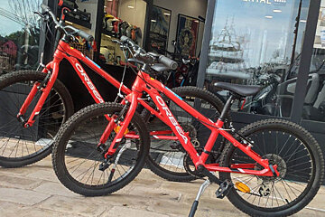 Two red orbea bikes are parked in front of a store