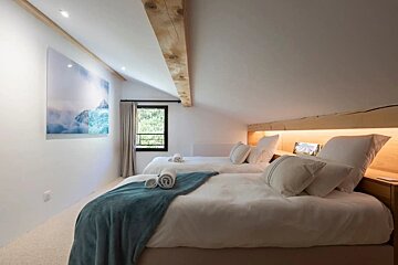 Cozy attic bedroom with two twin beds, a wooden beam, warm lighting, and a large mountain print on the wall.