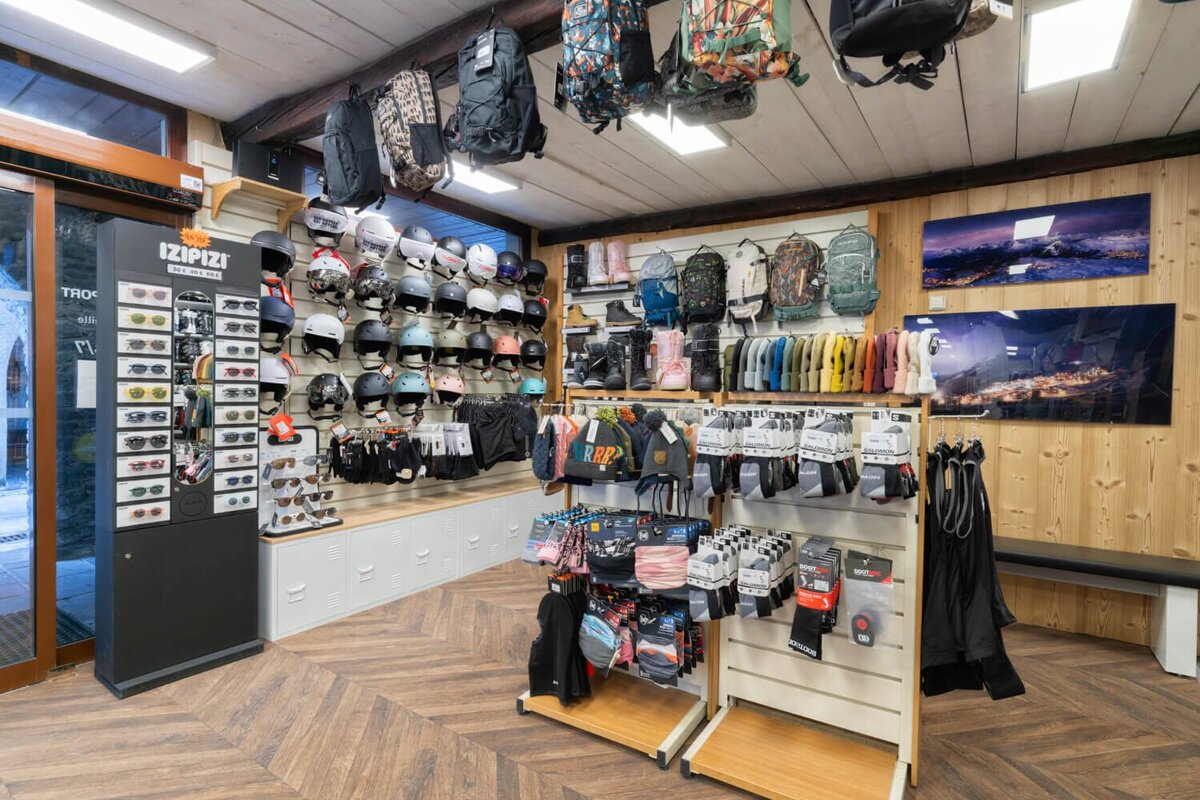 A brightly lit winter sports shop showcasing helmets, backpacks, boots, apparel, and sunglasses. The cozy interior features wood-paneled walls and floor.