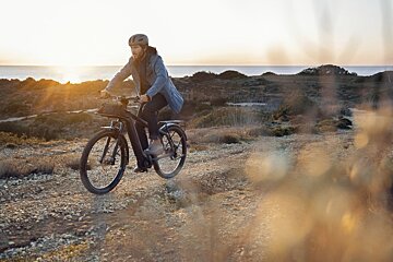 A man is riding a bike on a dirt road near the ocean