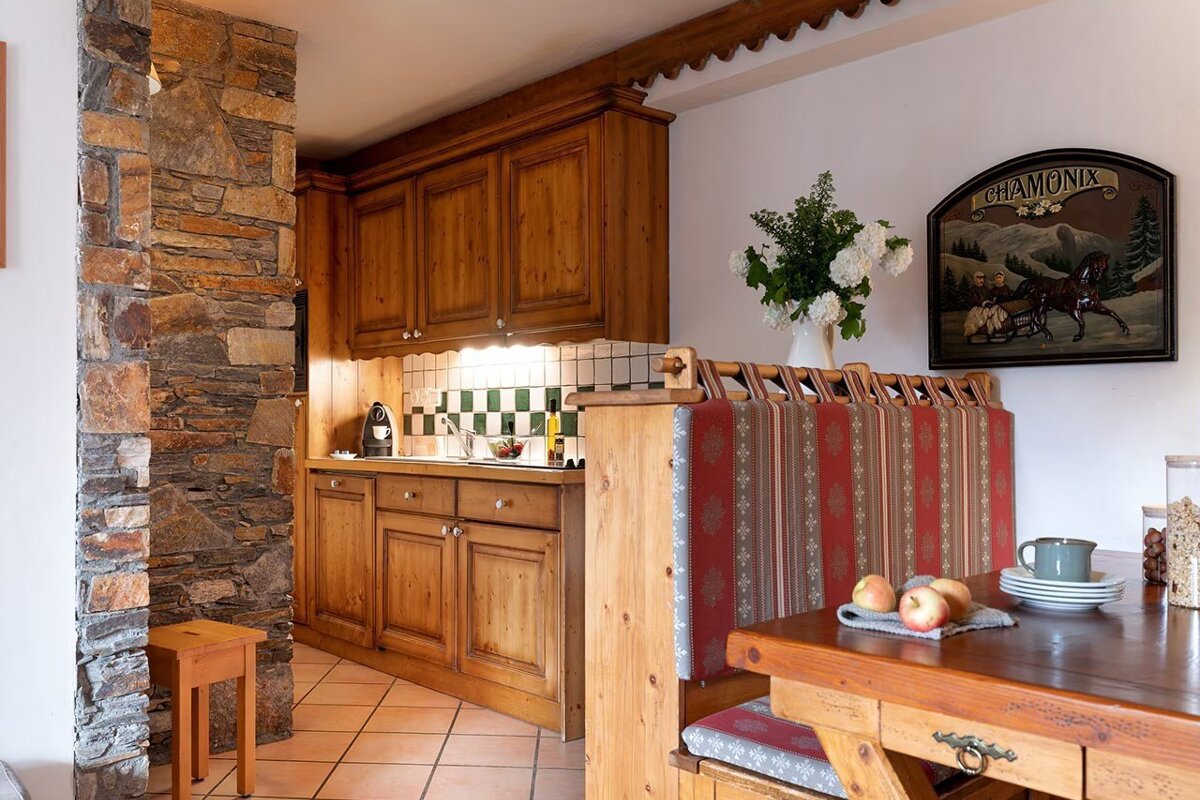 Rustic chalet-style kitchen and dining area with warm wooden cabinets, a stone wall, and a cozy bench seat.