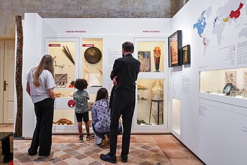 Visitors, including children, observe exhibits on protected species and cultural artifacts in a brightly lit museum hall with a world map.