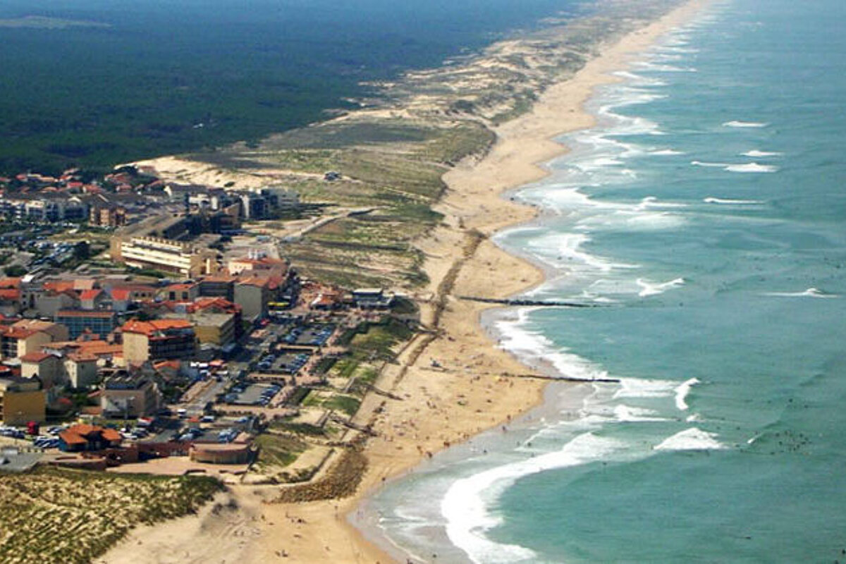 an aerial shot of a beach with a town behind