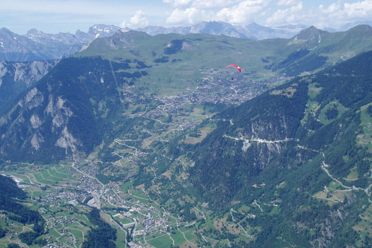 A paraglider is flying over a valley with mountains in the background