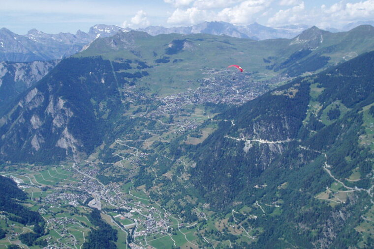 A paraglider is flying over a valley with mountains in the background
