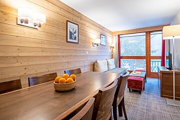 A bowl of oranges sits on a wooden table in a living room