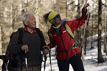 A man and a woman are hiking in the snow and the woman is wearing a red jacket that says esp