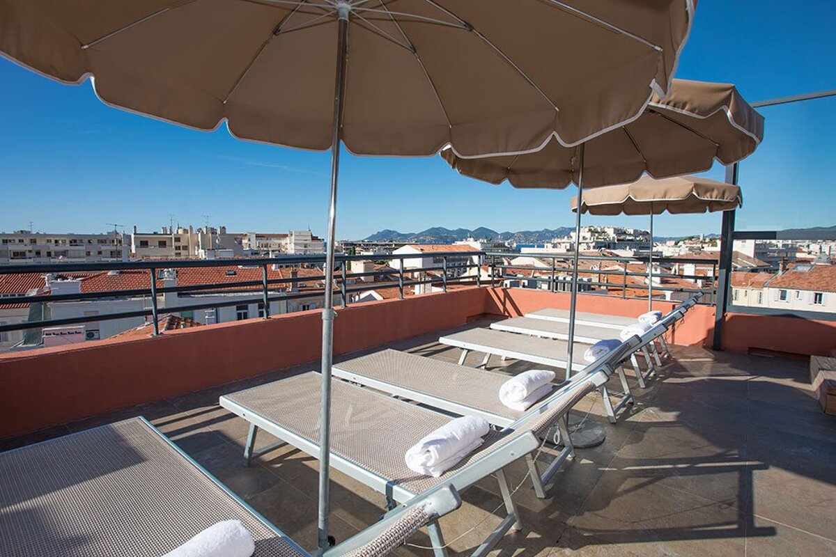 A row of lounge chairs under umbrellas on a balcony overlooking a city