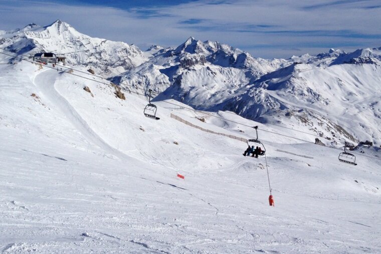 a few people on a chair lift over a wide piste