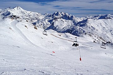 a few people on a chair lift over a wide piste