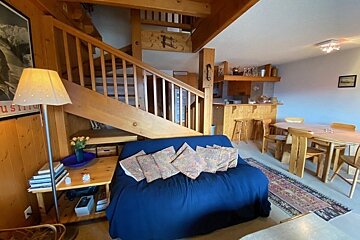 Cozy wooden cabin interior with a blue sofa, wooden stairs, and a dining table.