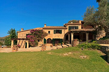 A large stone house with green shutters and purple flowers