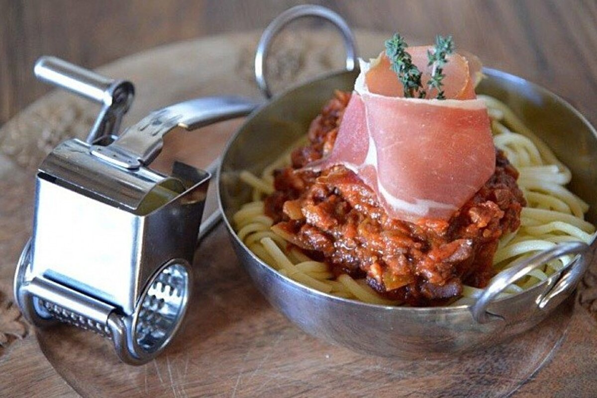 A bowl of spaghetti with meat and sauce next to a grater