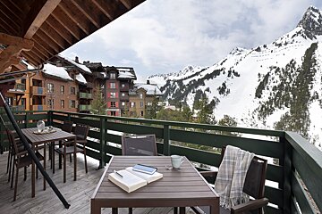 A book sits on a table on a balcony overlooking snowy mountains