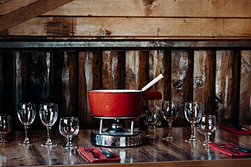 A red pot of fondue sits on a table with wine glasses