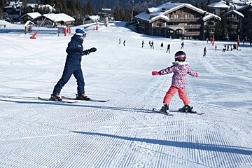 A person teaching a little girl how to ski on a snowy slope