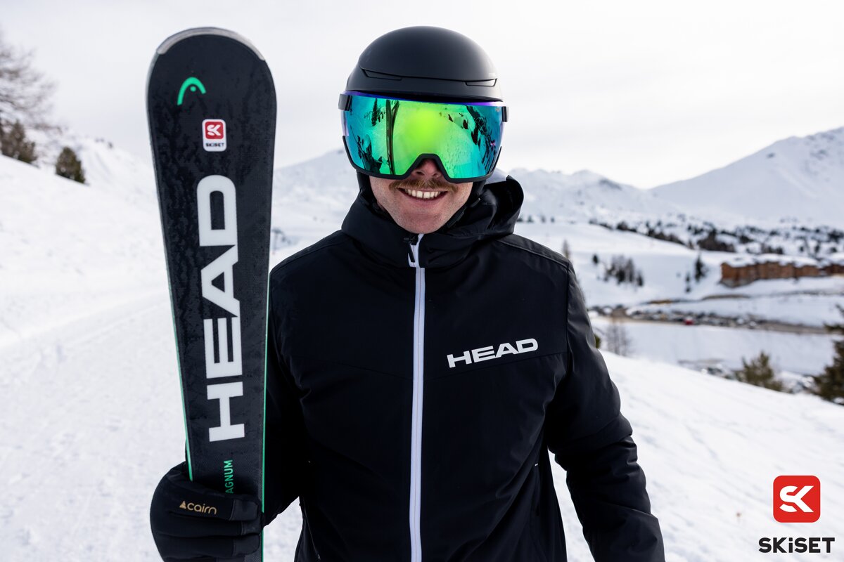 A man wearing a head jacket holds a pair of skis