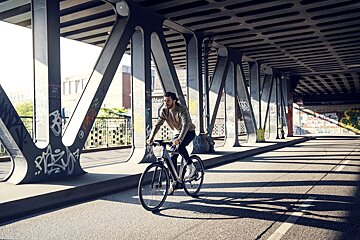 A man riding a bike under a bridge with graffiti on the wall