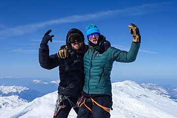 Two men standing on top of a snowy mountain with their arms in the air