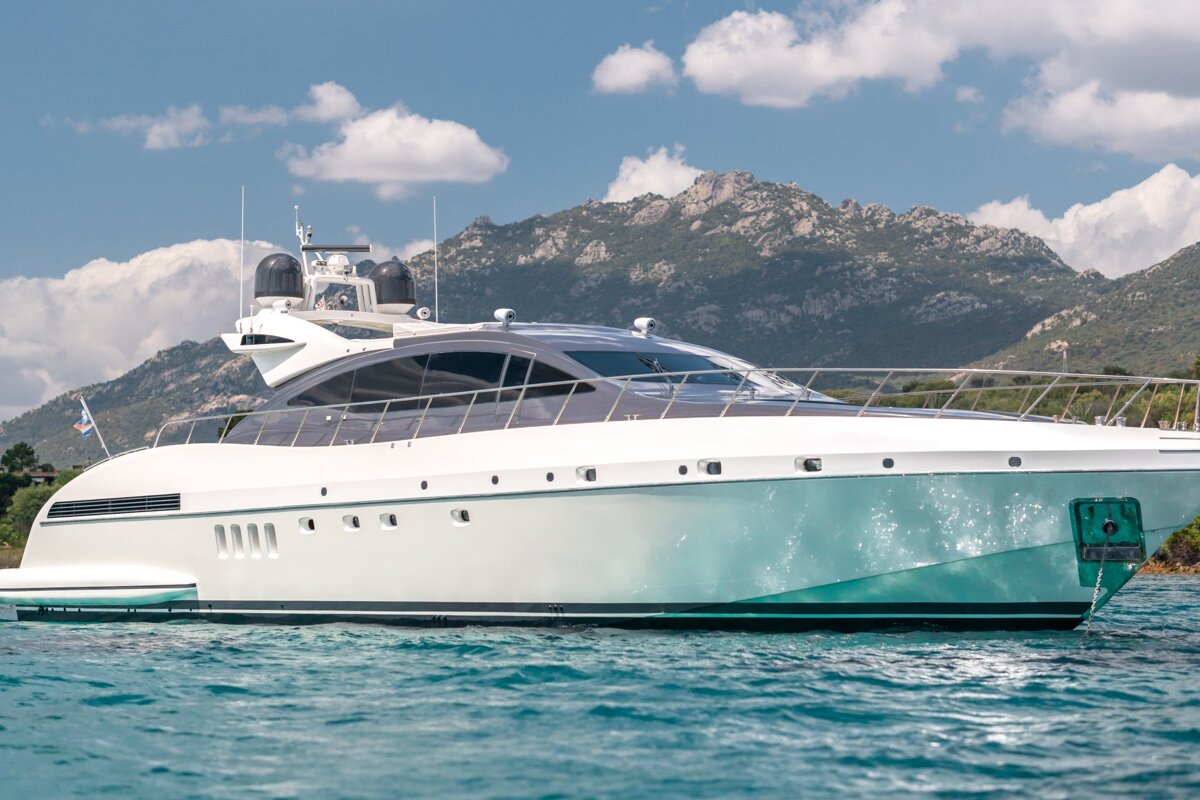 A large white yacht is in the water with mountains in the background